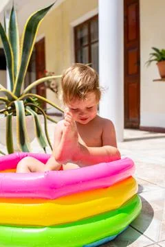 Cute child has fun in inflatable pool with toys in summer in backyard. Stockfoto's