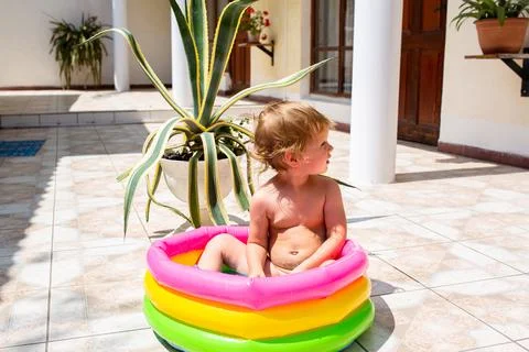 Cute child has fun in inflatable pool with toys in summer in backyard. 库存照片