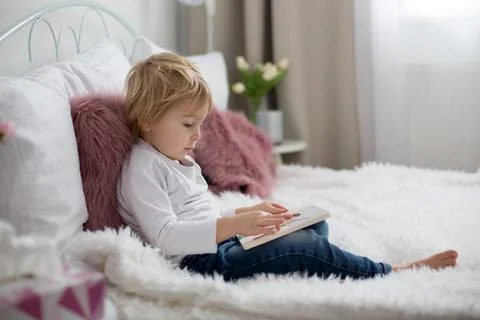 Cute child, lying in bed, reading book Stock Photos