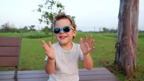 Cute child playing and making faces wearing sunglasses in park Stock Footage 303623874