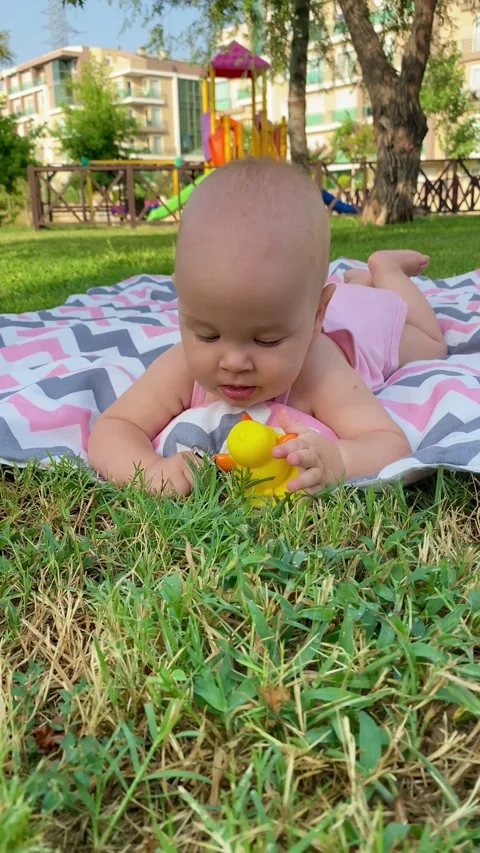 Cute child playing with a rubber ducky lying on a blanket on the grass in the Stock Footage 279919035