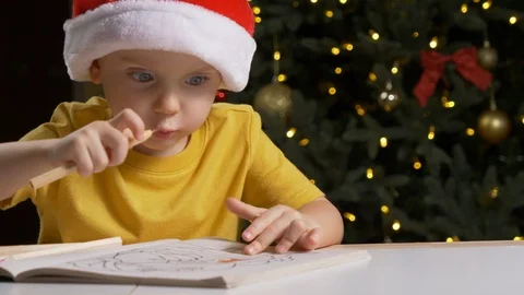 Cute child in Santa Claus hat is drawing with pencils in coloring book 库存影片 123201847