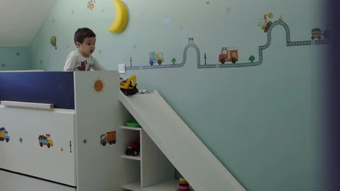Cute child sitting on his bed in kids room and playing with excavator toy and Stock Footage 104989023