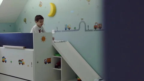 Cute child sitting on his bed in kids room and playing with police car toy and Stock Footage 104989049