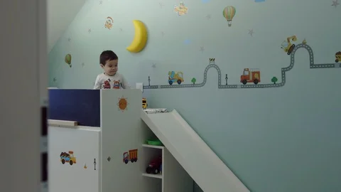 Cute child sitting on his bed in kids room and playing with truck toy and make Stock Footage 104989075
