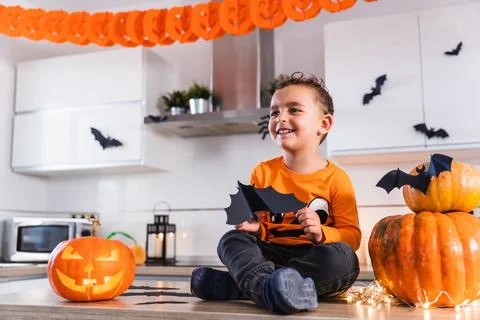 Cute child sitting at the kitchen table dressed as a pumpkin playing with bats Stock Photos