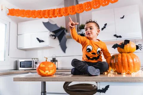 Cute child sitting at the kitchen table dressed as a pumpkin playing with bats Stock Photos