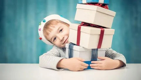 Cute child sitting at the table with stack of giftboxes Stock Photos