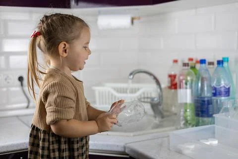 Cute child sorting plastic in the kitchen. The daughter follows the example of Stock-Fotos