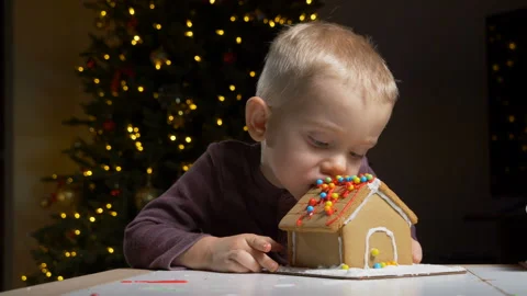 Cute child trying to eat, bite decorated gingerbread cookie house Stock Footage 122570653