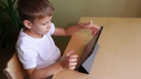 Cute child use tablet sitting by desk at home Stock Footage 143656920