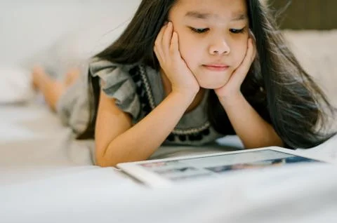 Cute child using a tablet and smiling while sitting on sofa at home Stock Photos