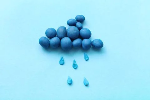 Cute cloud with rain drops made of plasticine on blue background Stock Photos