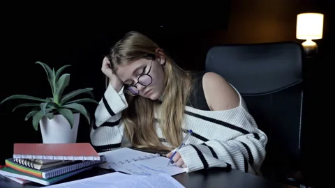 Cute college student stayed up late doing her homework. Tired girl wants to Stock Footage 232296036