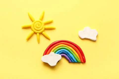 Cute composition with rainbow, sun and clouds made of plasticine on yellow ba Stock Photos
