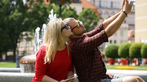 Cute couple having fun while doing photos on smartphone next to the fountain Stock Footage 77477083