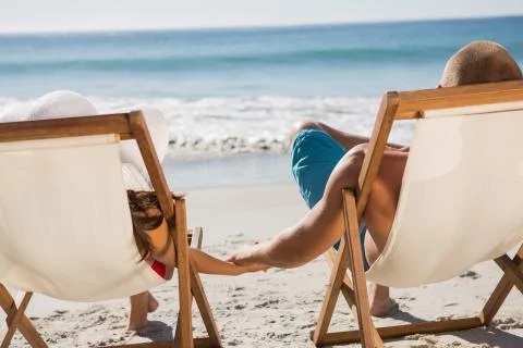 Cute couple holding hands while lying on their deck chairs Stock Photos