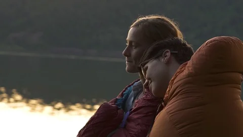 Cute Couple Relax In Their Sleeping Bags And Enjoy Sunset At River, They Cuddle Stock Footage
