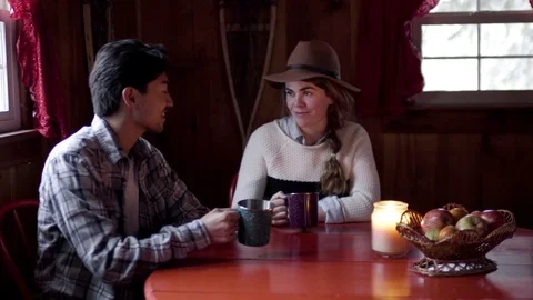 Cute Couple Sit At Kitchen Table In Cozy Cabin, They Cheers With Enamel Mugs Stock Footage 73083180