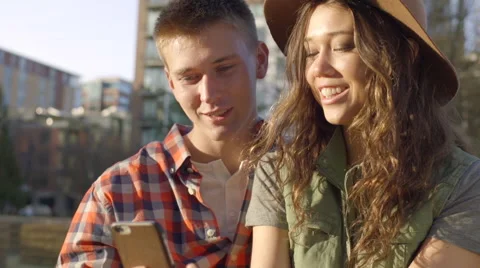 Cute Couple Sit On A Park Bench And Look Through Their Photos On A Smartphone Stock Footage 61019977