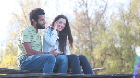 Cute couple sitting on bench and listening to music on shared earphones Stock Footage 59555252