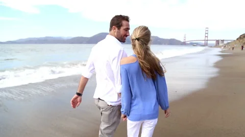 Cute couple walking down baker beach with golden gate in background Stock Footage 41969664