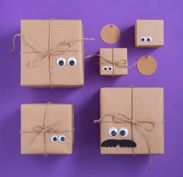 Cute craft gift boxes and gifttags laid out in order on violet background. Stock Photos