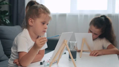 Cute curious sisters writing or working on paper in kindergarten with paintbrush Stock Footage 282659717