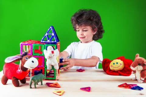 Cute curly boy in a white t-shirt is building a wall of a house with friends. Fotos de archivo