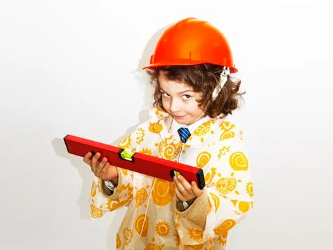 A cute curly-haired boy builder in a raincoat holding a building level.Forema Stock Photos
