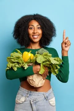 Cute curly haired dark skinned woman, pointing finger up with cheerful smile Stock-Fotos