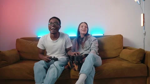 A cute dachshund is lying on a couch between a mixed young couple who are Stock-Footage 173016946