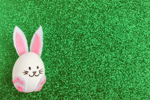 Cute Easter bunny decorated from egg on green glitter background. Copy space Stock Photos