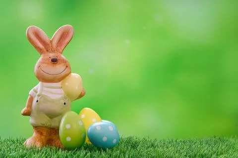 Cute Easter bunny in pants on the grass next to the painted bright eggs. Stock Photos