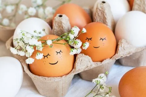 Cute easter eggs with funny faces in brown box with flowers background. Hap.. Stock Photos