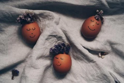 Cute Easter eggs with a painted face with a flower wreath on the linen cloth Stock Photos