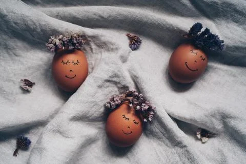 Cute Easter eggs with a painted face with a flower wreath on the linen cloth Stock Photos