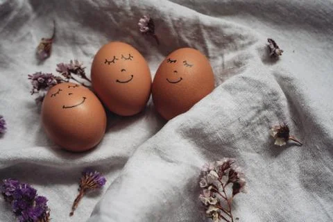 Cute Easter eggs with a painted face and dried flowers on the linen cloth. Flat Stock Photos