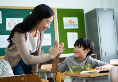 Cute elementary school boy and Asian female Teacher high five gesture team in Stock-Fotos