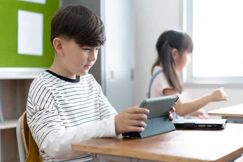Cute elementary school boy using digital tablet at desk in classroom. Educati Stock Photos