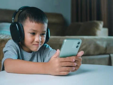 Cute elementary school boy wearing headphones holding a smartphone. Boy stu.. 스톡 사진