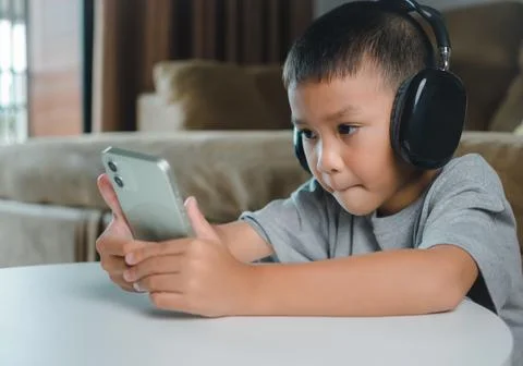 Cute elementary school boy wearing headphones holding a smartphone. Boy stu.. Stock Photos