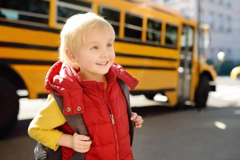 Cute elementary student with schoolbag on background of usa yellow school bus Foto stock