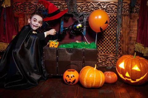 Cute emotional boy in vampire costume takes out candy from the treasure chest Stock Photos