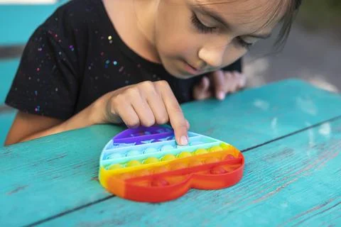 Cute faceless child playing with the Pop It fidget. The girl looks at the toy Stock Photos