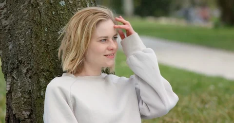 Cute female sitting next to a tree in a sunny park Stock Footage 107156458