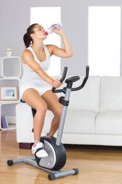 Cute fit woman drinking water while training on an exercise bike Stock Photos