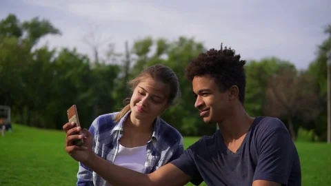 Cute friends resting in a park, sitting on the grass, looking at the smartphone Stock Footage 80979545