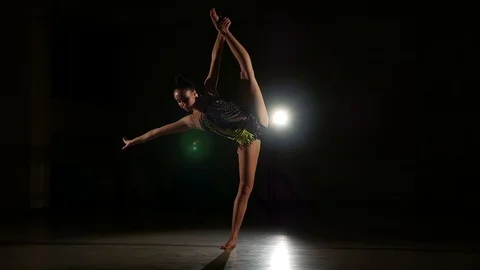 Cute girl athlete performs elements of rhythmic gymnastics in dark gym Stock Footage 104689613