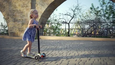 Cute girl in blue dress having fun riding the scooter slow motion Stock Footage